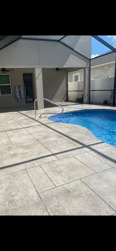 Light stone-pattern stamped concrete pool deck and covered patio beside a screened pool in Westchase, FL